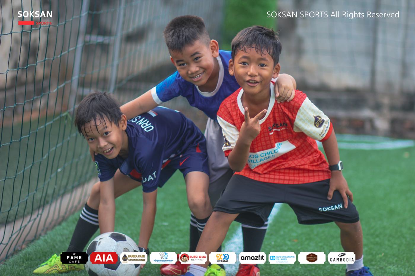 Three young players grinning together over a football